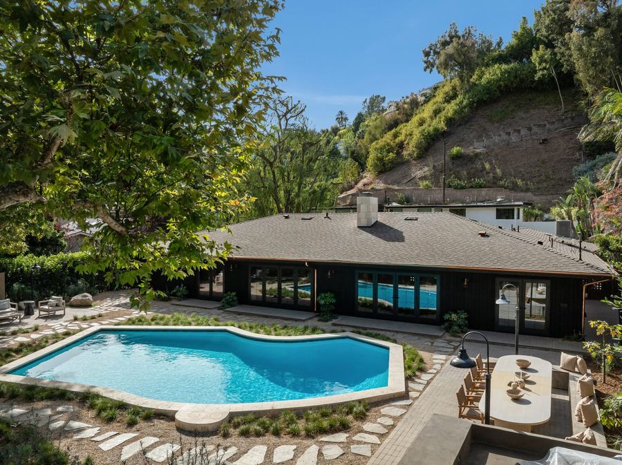 Backyard pool with flagstone paths, ornamental grasses and an outdoor dining terrace beside a dark ranch-style home