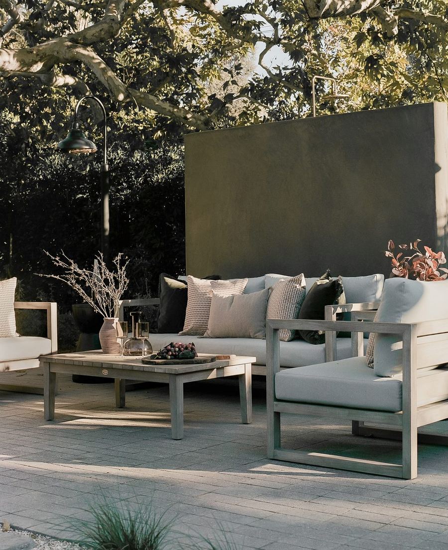 Paver patio with a teak sofa and chairs set against a plaster privacy wall under tree canopy