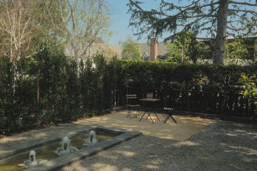 Gravel courtyard with a rectangular stone fountain, bistro seating and a tall hedge screen